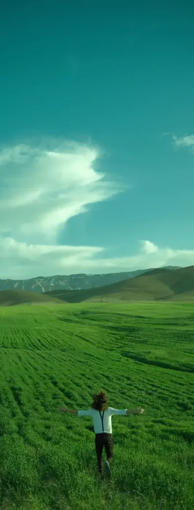 A man running through a wide-open field with his arms extended outwards.